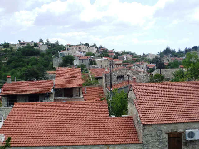 Het wijndorp Lofou op een groene helling achter Limassol, met stenen huizen en rode pannendaken Het wijndorp Lofou op een groene helling achter Limassol, met stenen huizen en rode pannendaken